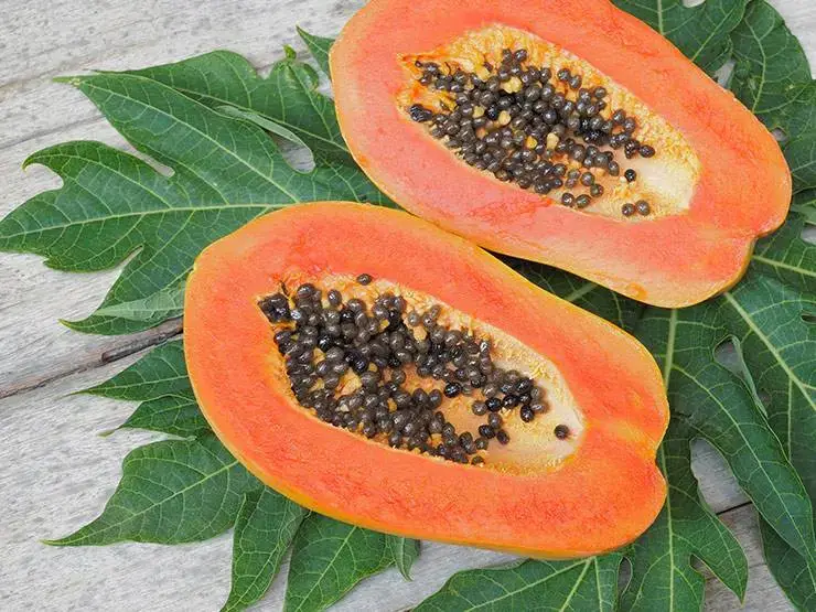 Two slices of ripe papayas with seeds and leaves