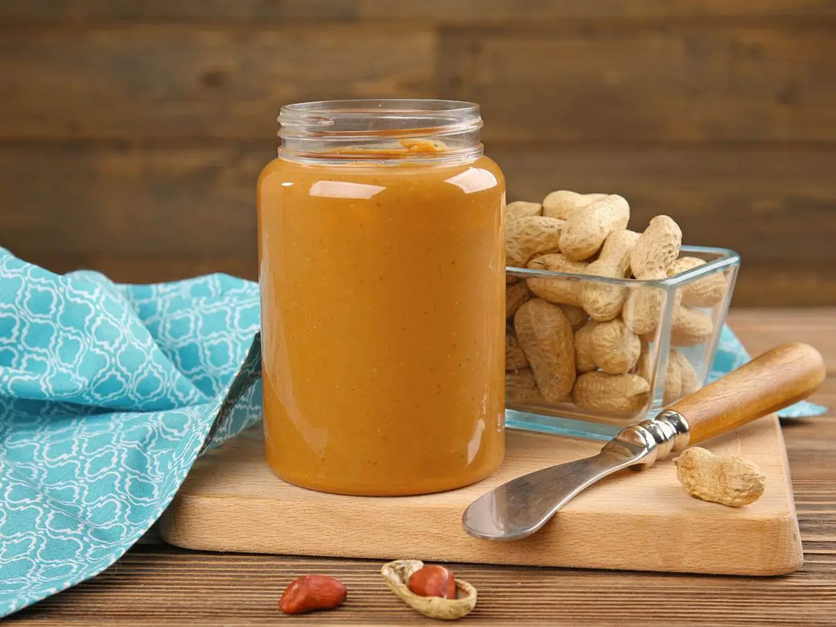 A jar of peanut butter beside a bowl of peanuts